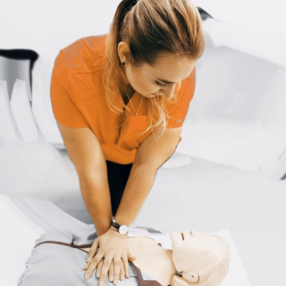 A nurse teacher with orange uniform gives first aid to a fake doll